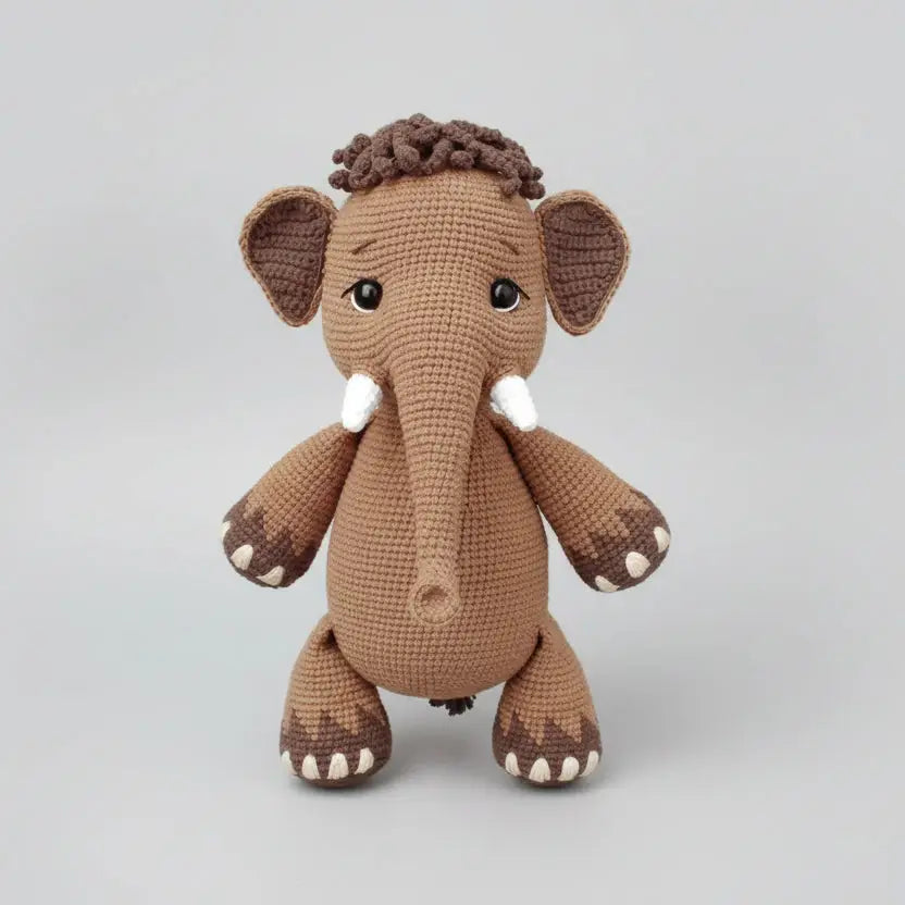 Crocheted toy mammoth named Peanut on a wooden surface with yarn and patterns displayed.