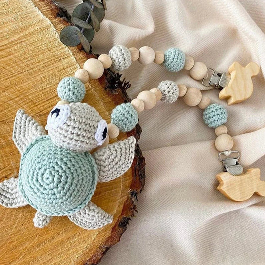 Crocheted blue-gray turtle and wooden bead pacifier clip on textured background