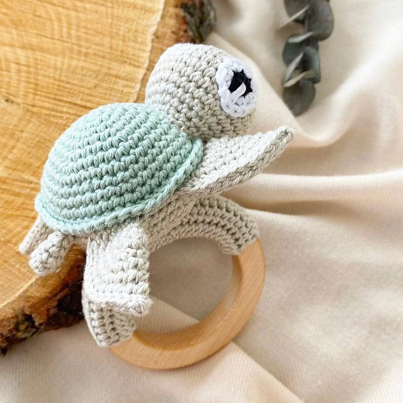 Crocheted sea turtle baby rattle with wooden teething ring on soft fabric