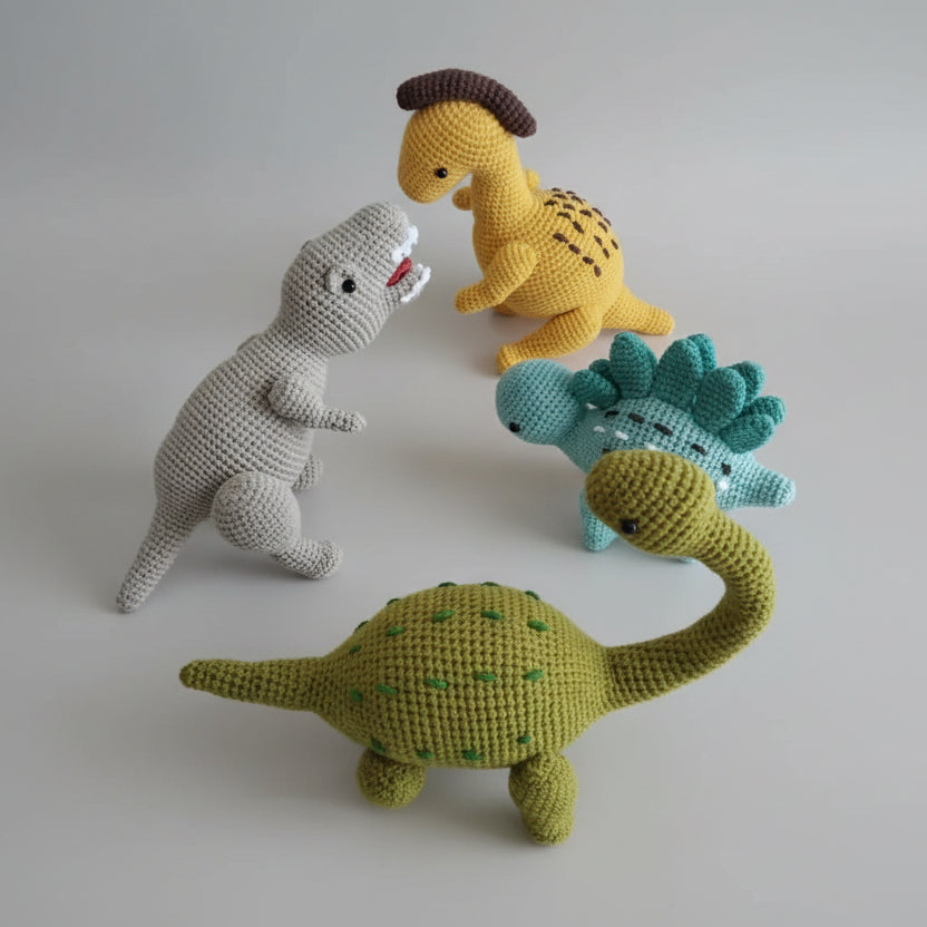Crocheted dinosaurs in yellow, green, blue, and gray, posed playfully on a white surface
