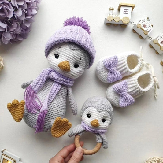 Crocheted penguin plushie with purple hat, scarf, baby booties, and wooden toy train