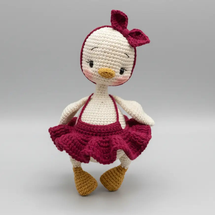 Crocheted bird doll in burgundy skirt with pink bow, standing sweetly against gray background