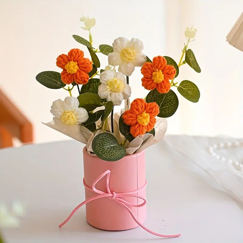 Orange and white crochet flowers in a pink tied container with green leaves
