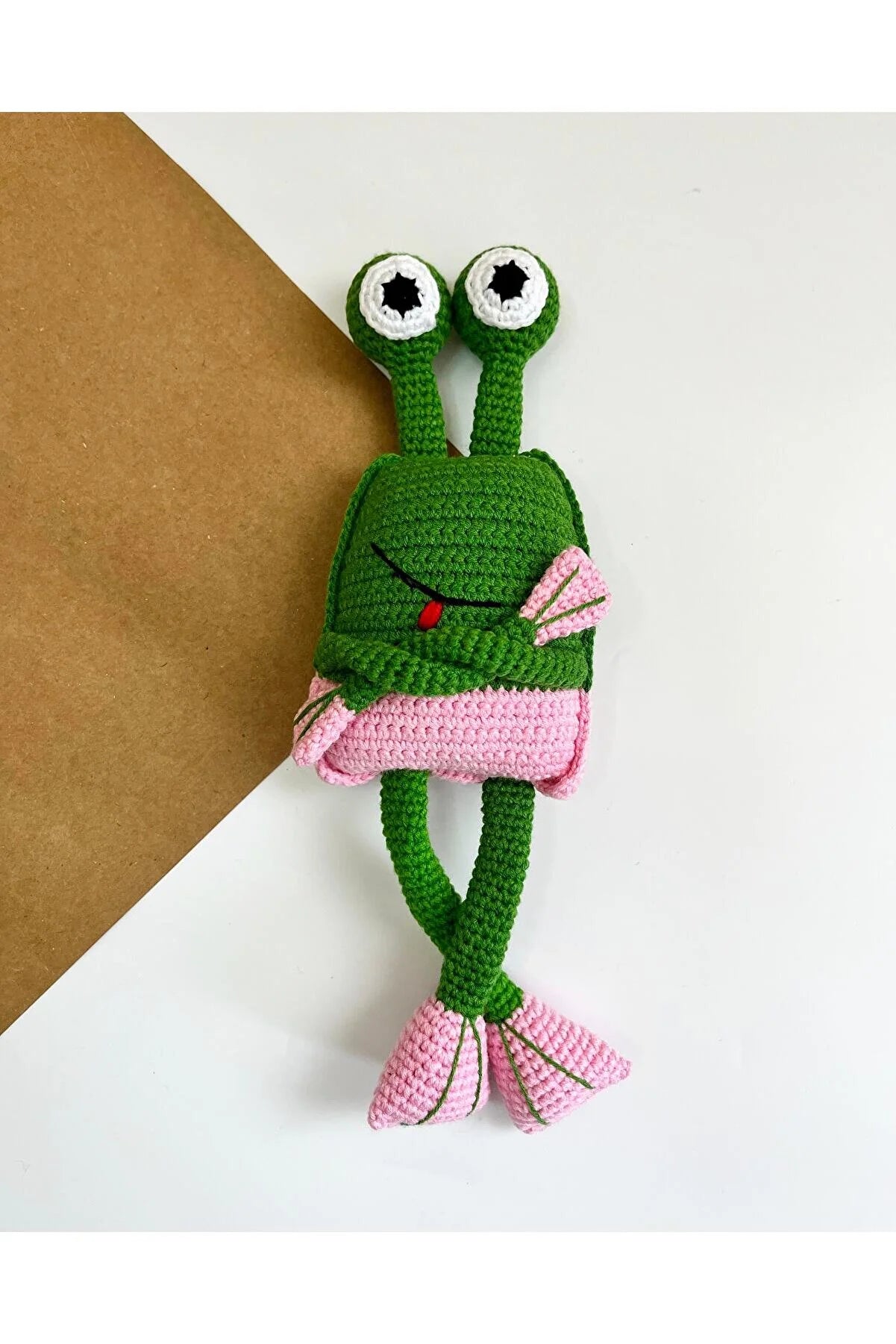 Crocheted green and pink alien-like creature with large googly eyes and long limbs