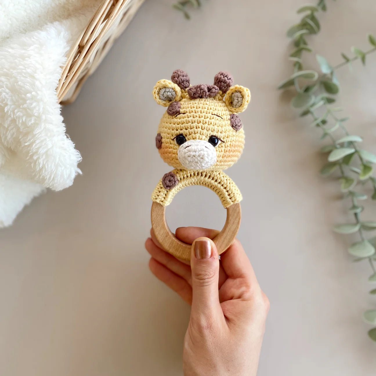 Crocheted giraffe baby teething ring held in hand, with wooden ring and soft yarn details