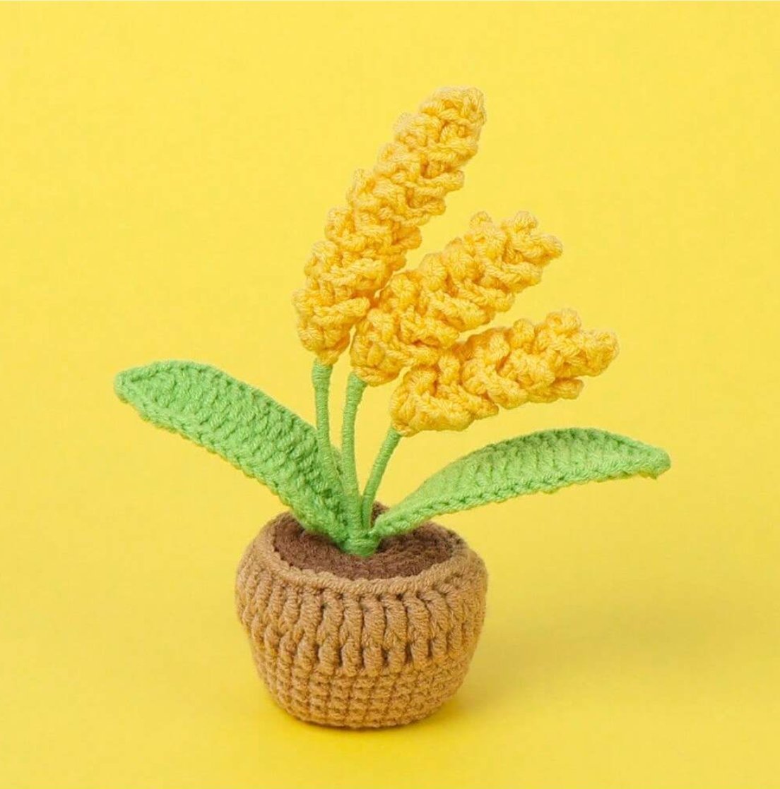 Crocheted yellow flowers with green leaves in a brown textured pot against yellow background