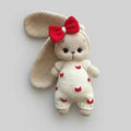 Crocheted bunny with red bow and heart-patterned white outfit on gray background