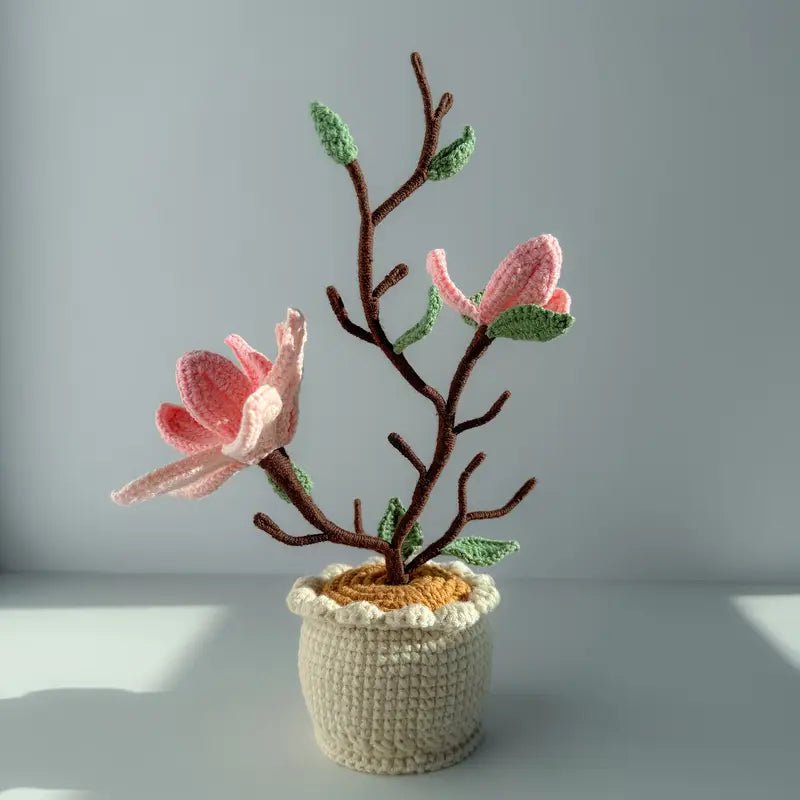 Crocheted magnolia tree with pink flowers in a cream-colored pot against a gray background