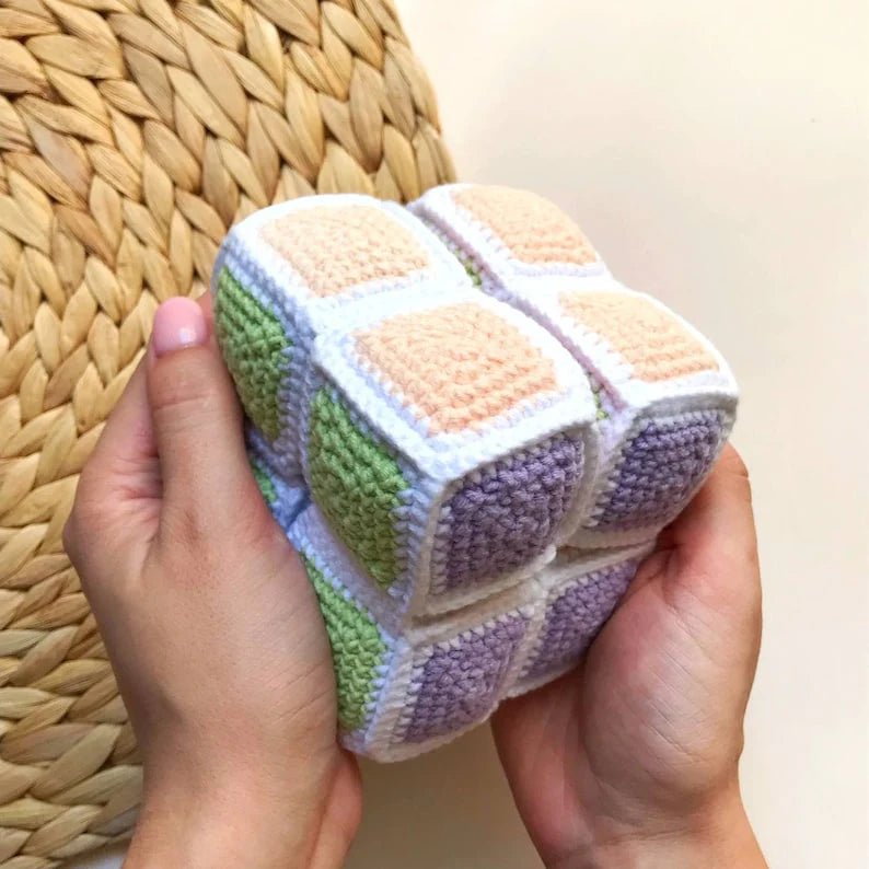 Crocheted soft cube with pastel green, purple, white, and peach colored squares