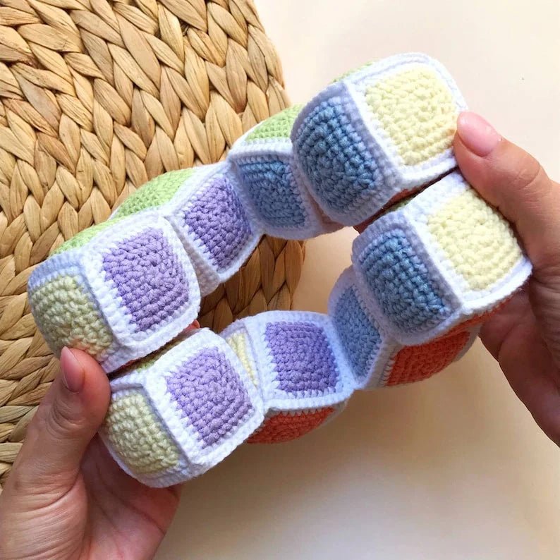 Crocheted colorful cube toy with pastel green, blue, purple, yellow, and white squares