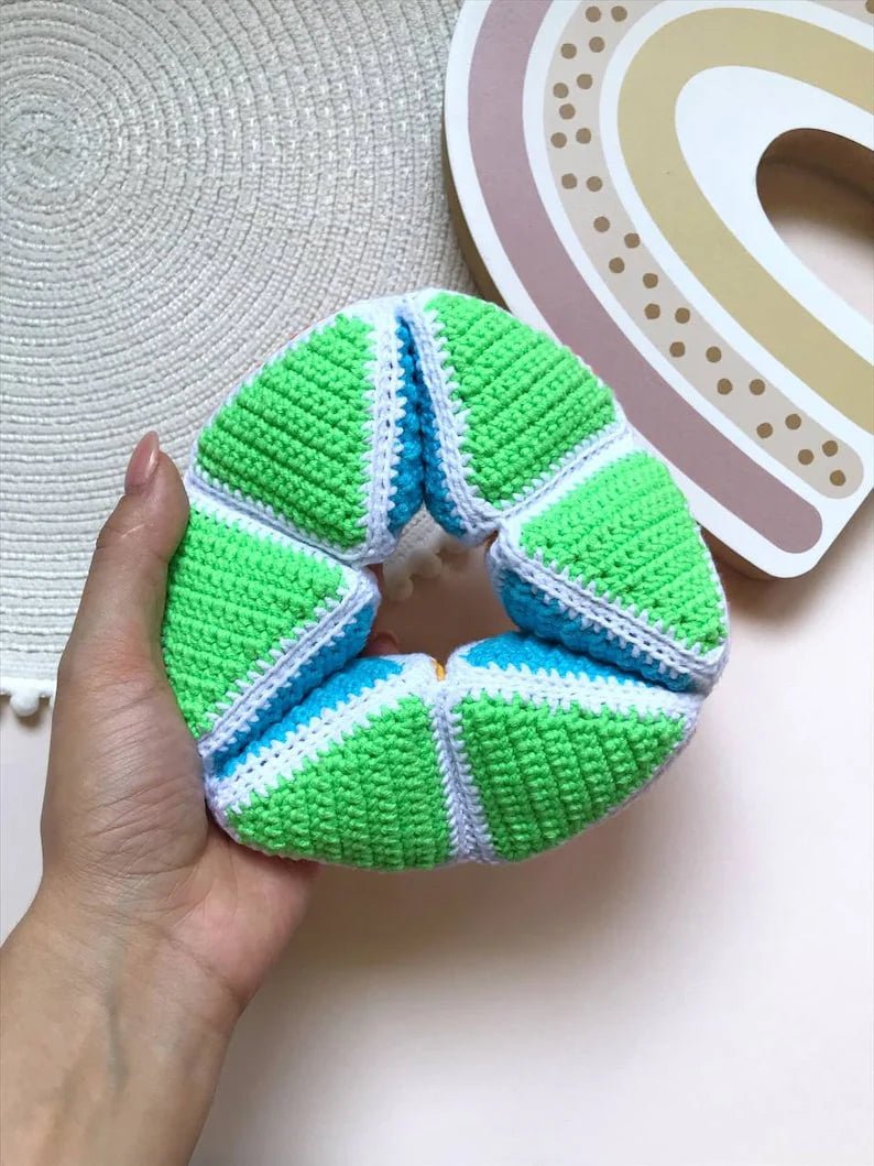 Crocheted donut-shaped object in green, blue, and white, held by a hand