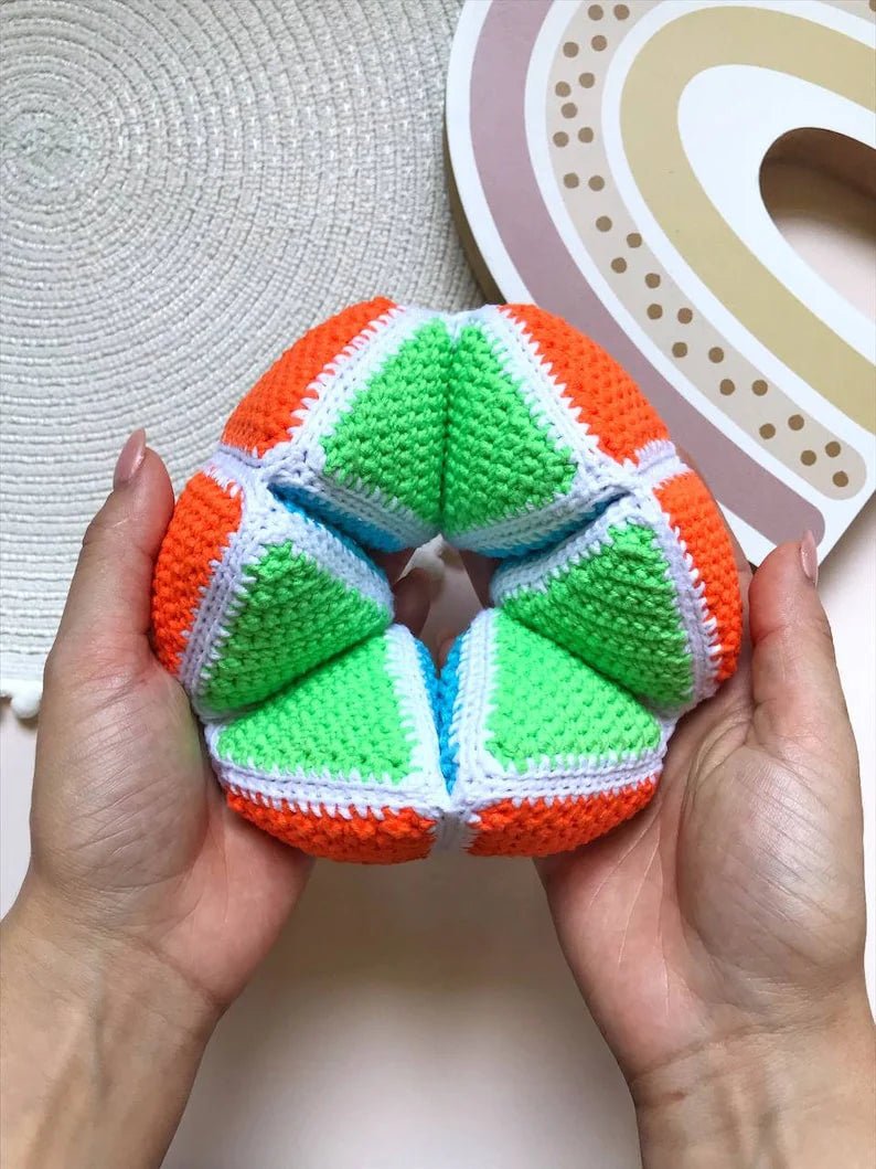 Crocheted colorful geometric ball with orange, green, and white sections held in hands