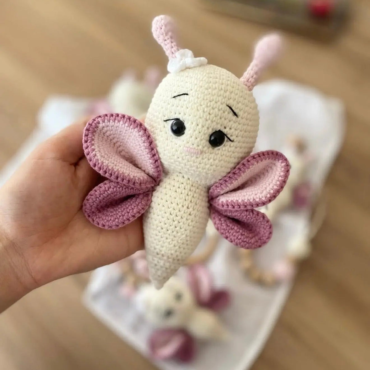 Crocheted pink and white butterfly toy held in a hand, with soft, detailed stitching