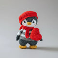 Crocheted penguin in red winter hat and scarf, gray and white with yellow beak