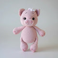 Pink crocheted pig stuffed animal with a white flower on its ear