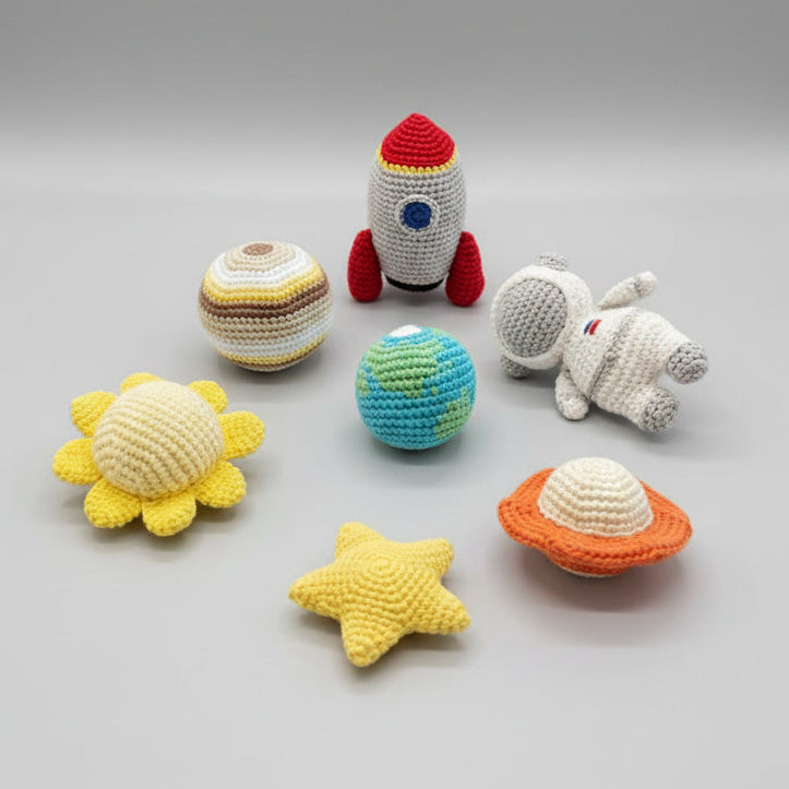 Collection of colorful crochet toys including a rocket, planets, and a star on a dark surface.