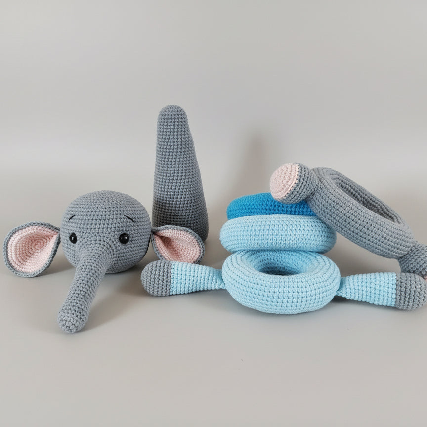 Crocheted gray and blue elephant toy with stacking rings on wooden surface