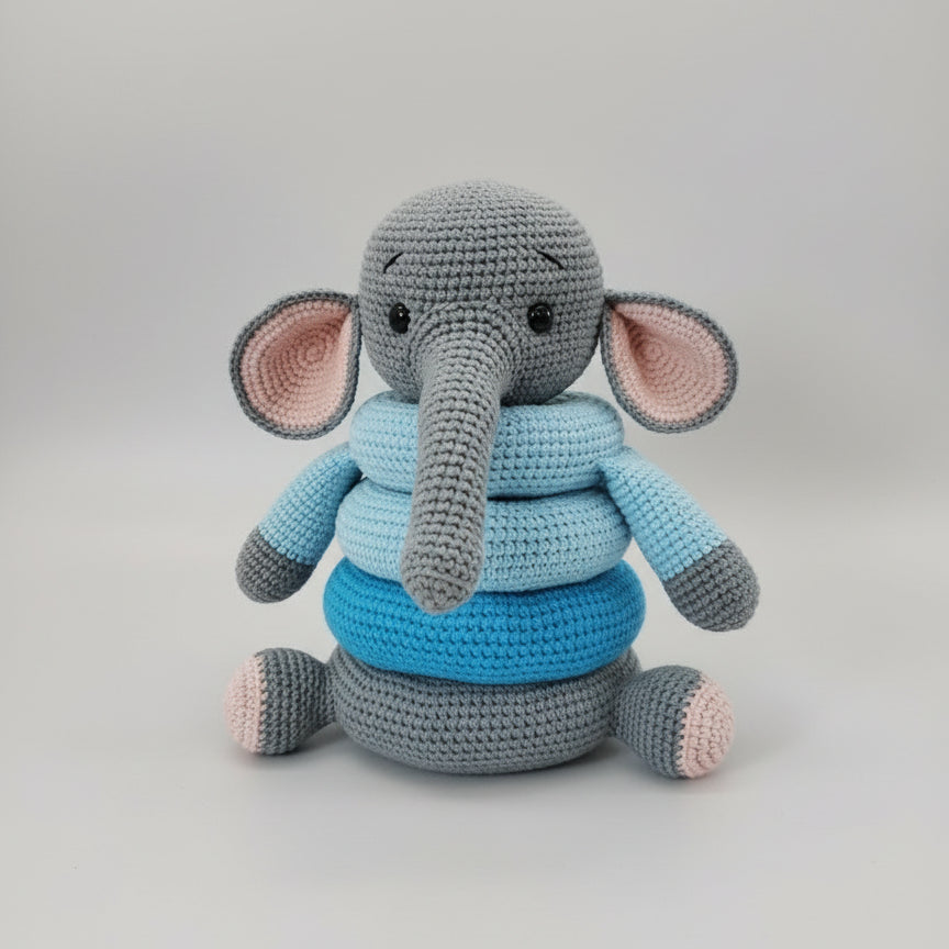 Crocheted gray elephant plush toy with blue and pink shades, sitting on wooden surface