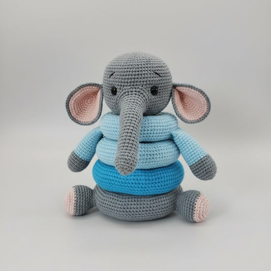 Crocheted gray elephant plush toy with blue and pink shades, sitting on wooden surface