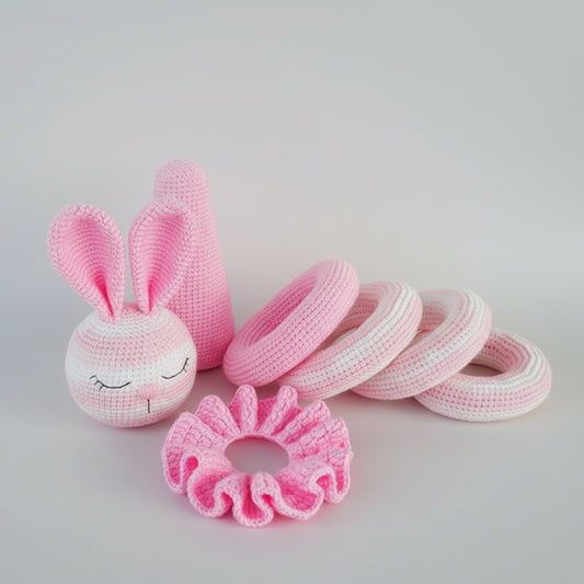 Crocheted pink bunny, rings, and flower on wooden surface, handmade baby toys