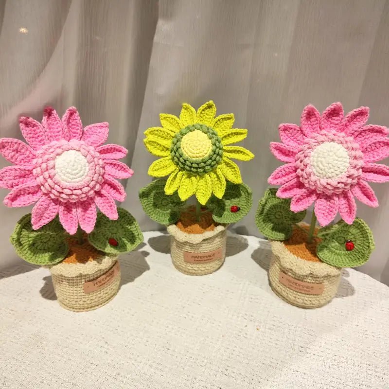 Three crocheted flowers in pink and yellow, potted in textured yarn containers with small ladybug details