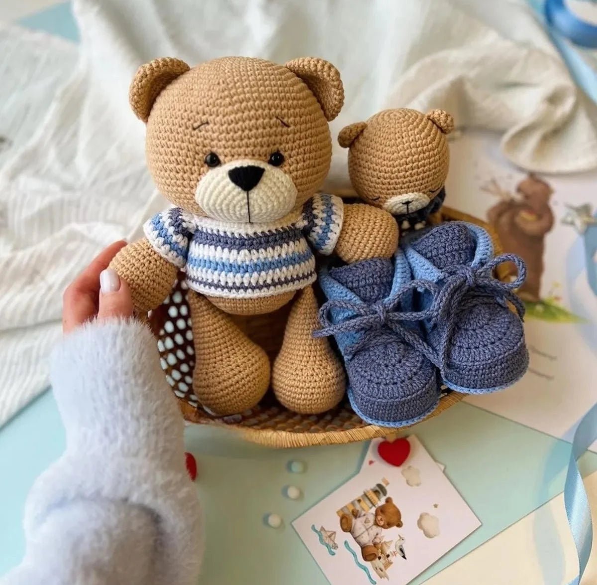 Crocheted teddy bear and baby booties on wooden surface with card and ribbons