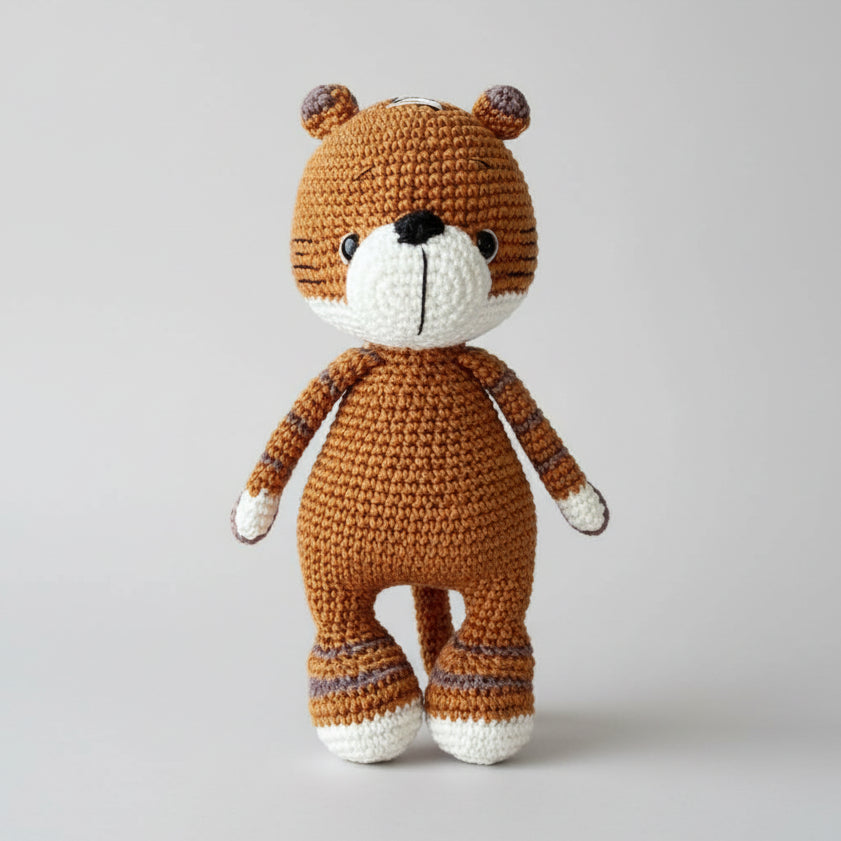 Crocheted brown teddy bear with white face, standing on a neutral background