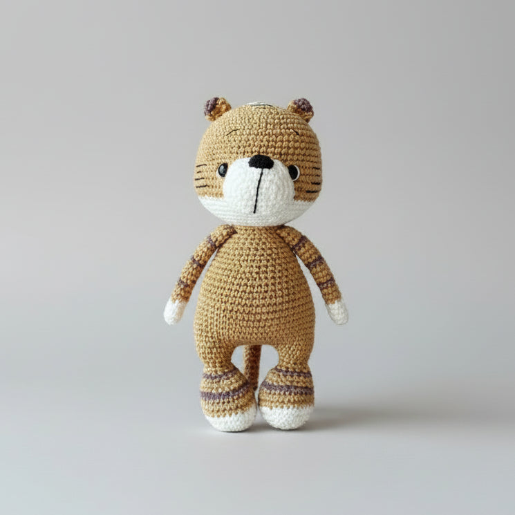 Crocheted teddy bear in tan and white, standing on a gray background