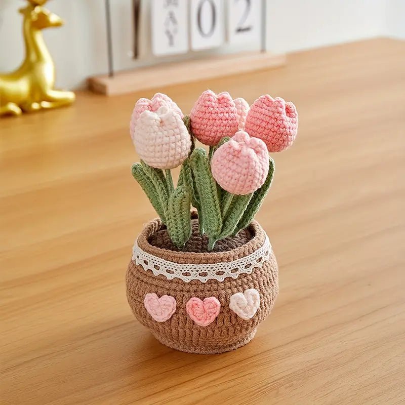 Crocheted pink tulips in a heart-decorated pot with lace trim on wooden surface