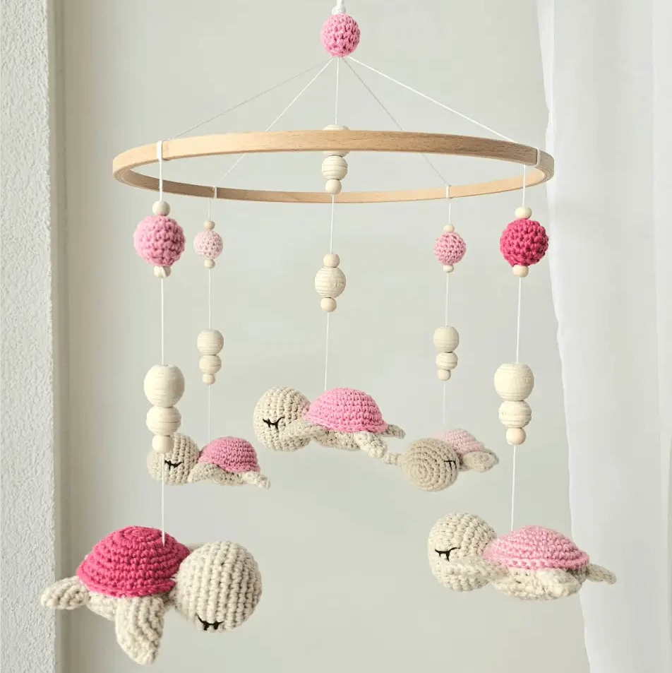 Crocheted baby mobile with sleeping pink and cream turtles hanging from wooden ring