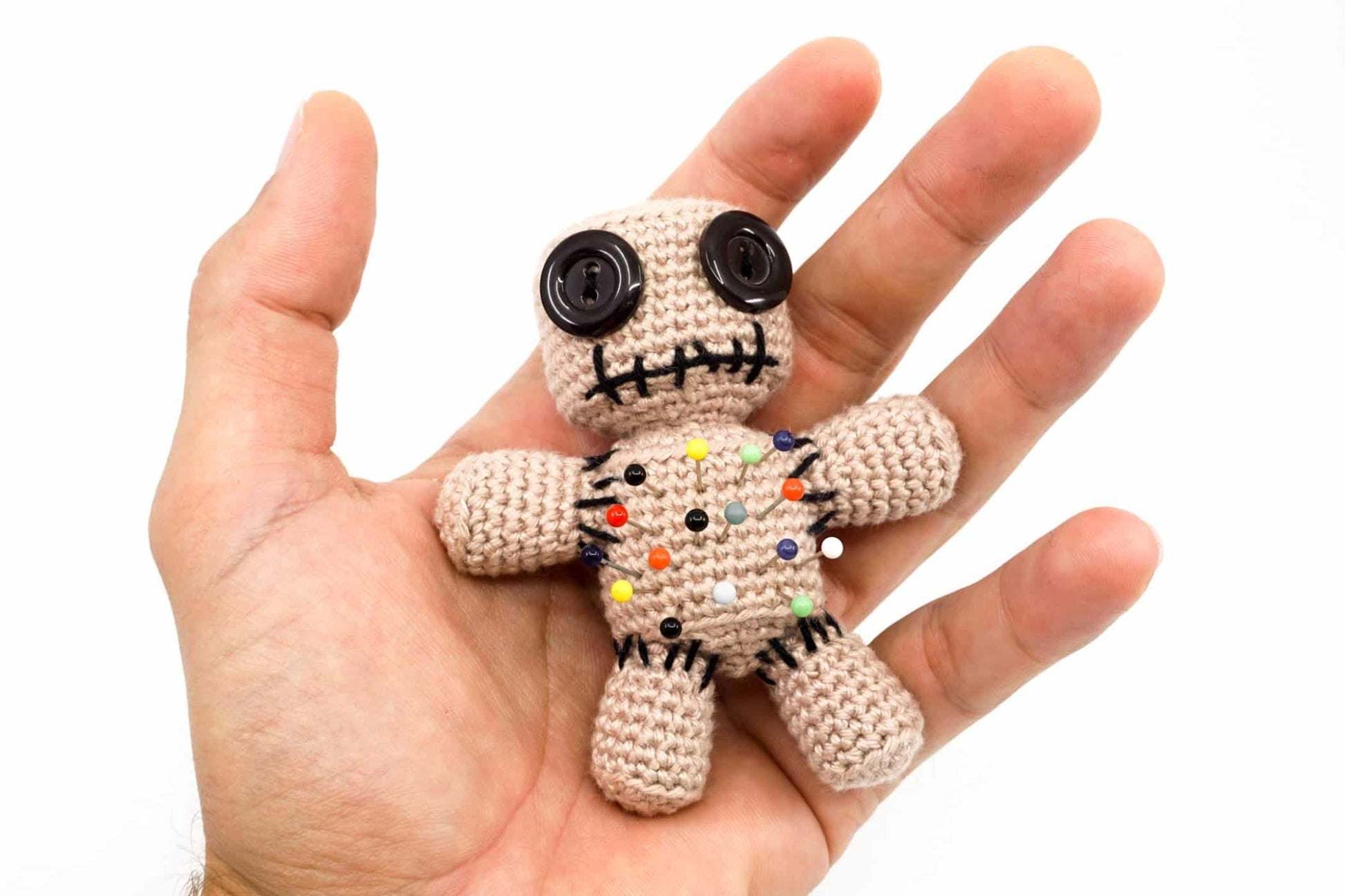 Crocheted voodoo doll with button eyes and colorful pins on an open palm