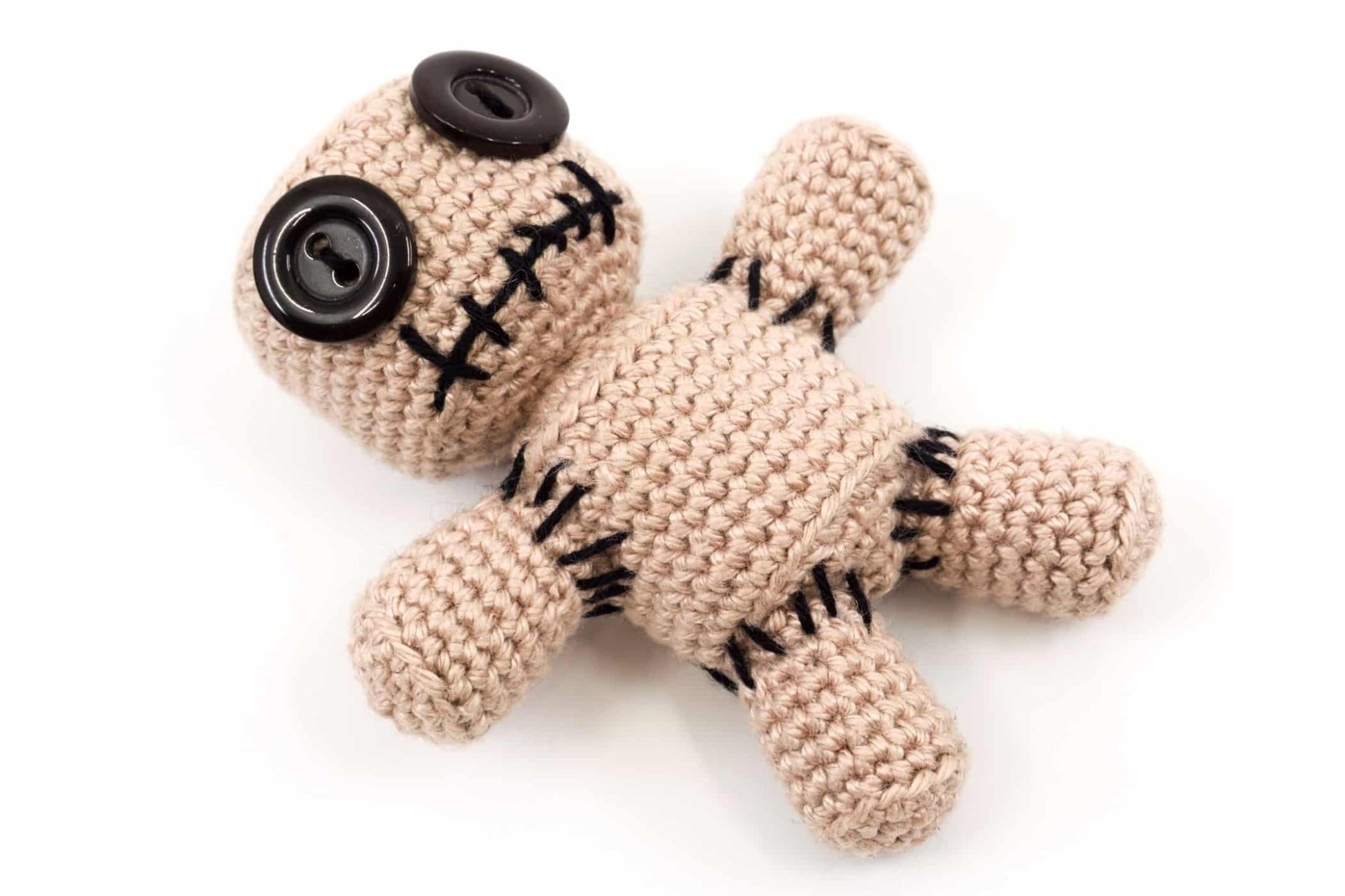Crocheted voodoo doll with black buttons and stitched details on beige yarn body