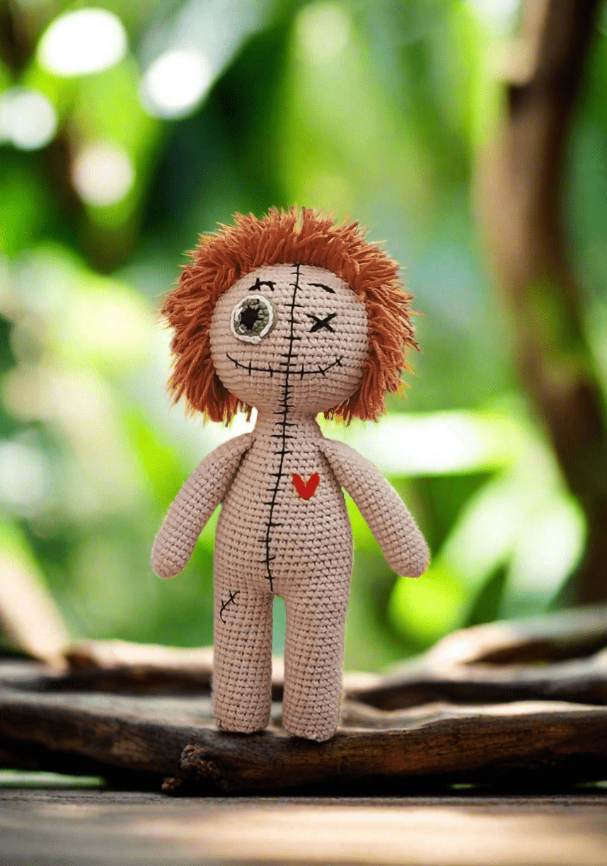 Crocheted voodoo doll with wild hair, sitting on a wooden branch with blurred green background