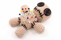 Crocheted voodoo doll with colorful pins and black buttons on beige yarn body