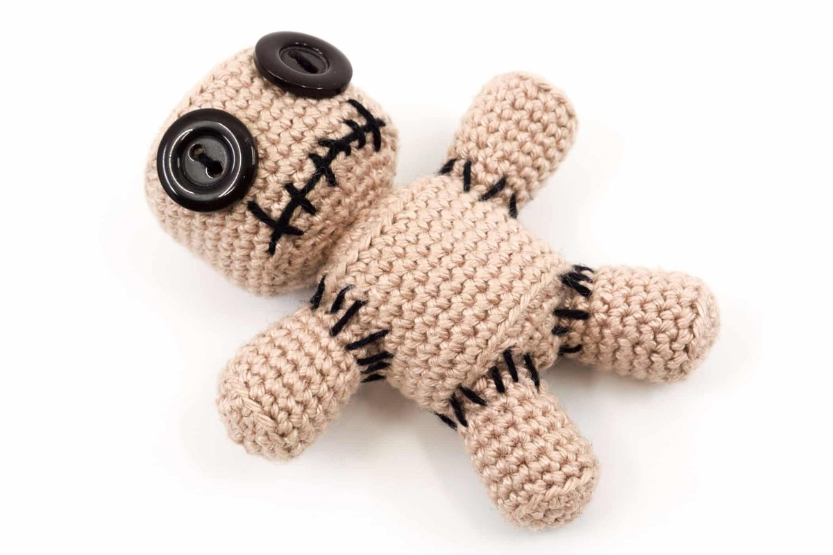 Crocheted voodoo doll with black buttons and stitched details on beige yarn body