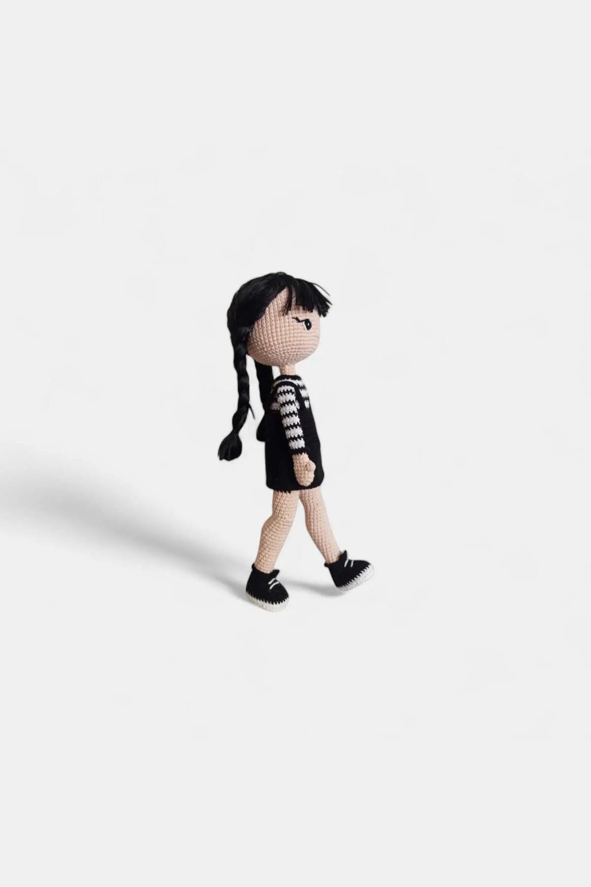 Crocheted doll with braids wearing black and white striped sweater and black shoes