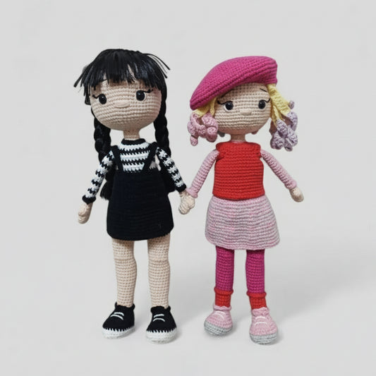 Two handmade crocheted dolls holding hands, wearing black and red outfits with berets