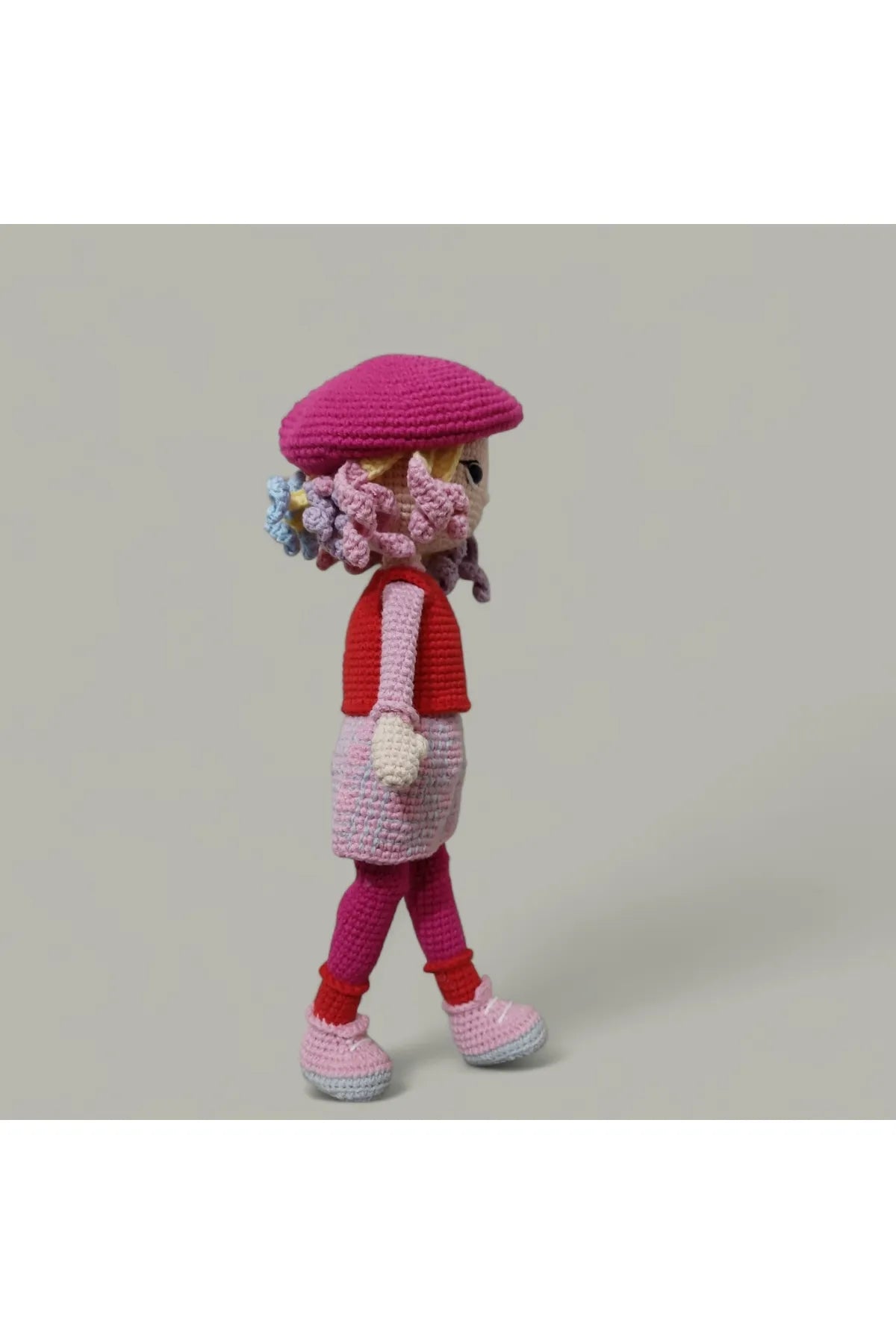 Crocheted doll in pink outfit with curly hair and beret, walking pose