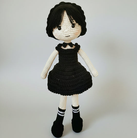 Crocheted doll with black dress and short hair, standing against neutral background