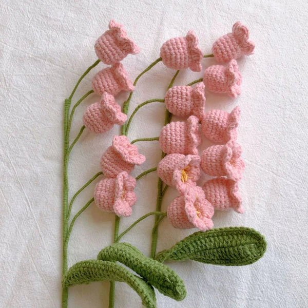 Crocheted pink bell-shaped flowers with green stems on white background