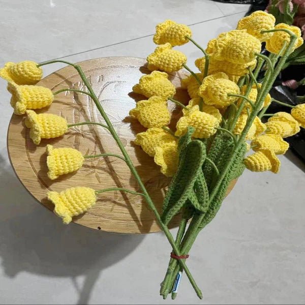 Crocheted yellow daffodils with green stems on a wooden surface, artfully arranged