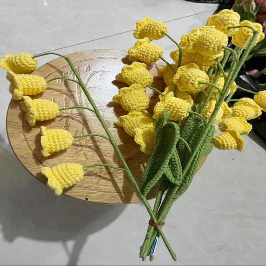 Crocheted yellow daffodils with green stems on a wooden surface, artfully arranged