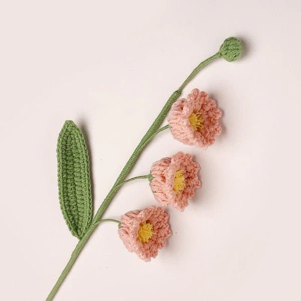 Crocheted pink flowers with green stem and leaf on soft background