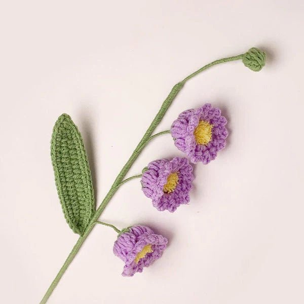 Crocheted purple flowers with yellow centers on green stem against white background