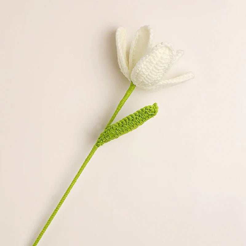 White crocheted flower with green stem against a neutral background