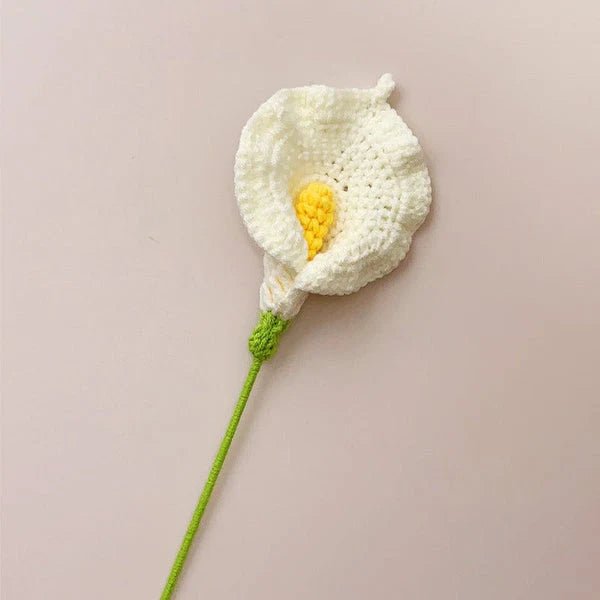 Crocheted white calla lily with yellow center and green stem on neutral background