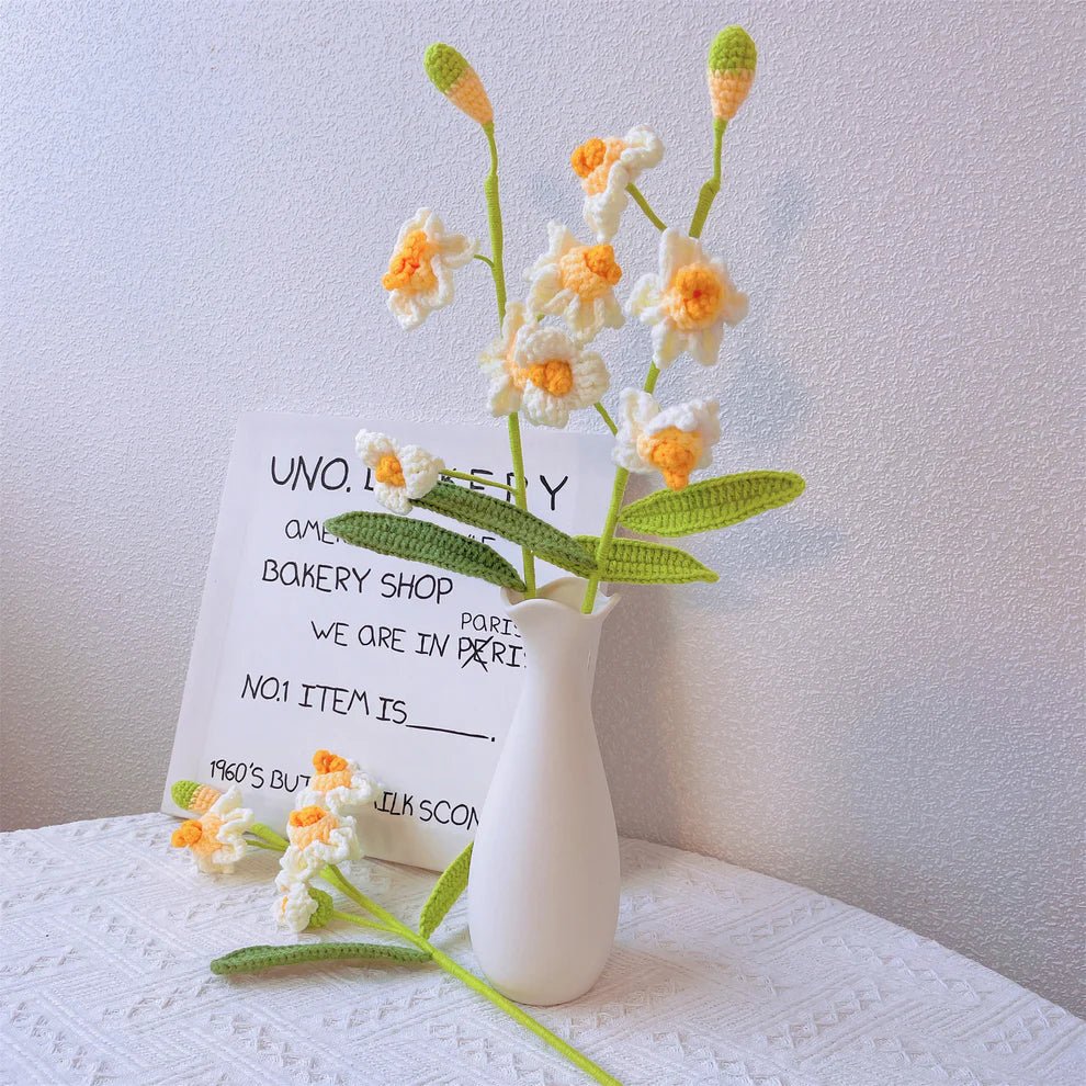 Crocheted white and yellow daffodils beside a handwritten bakery shop note in white vase