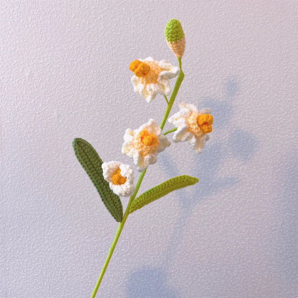 Crocheted white and yellow flower with green stem and leaves on textured background