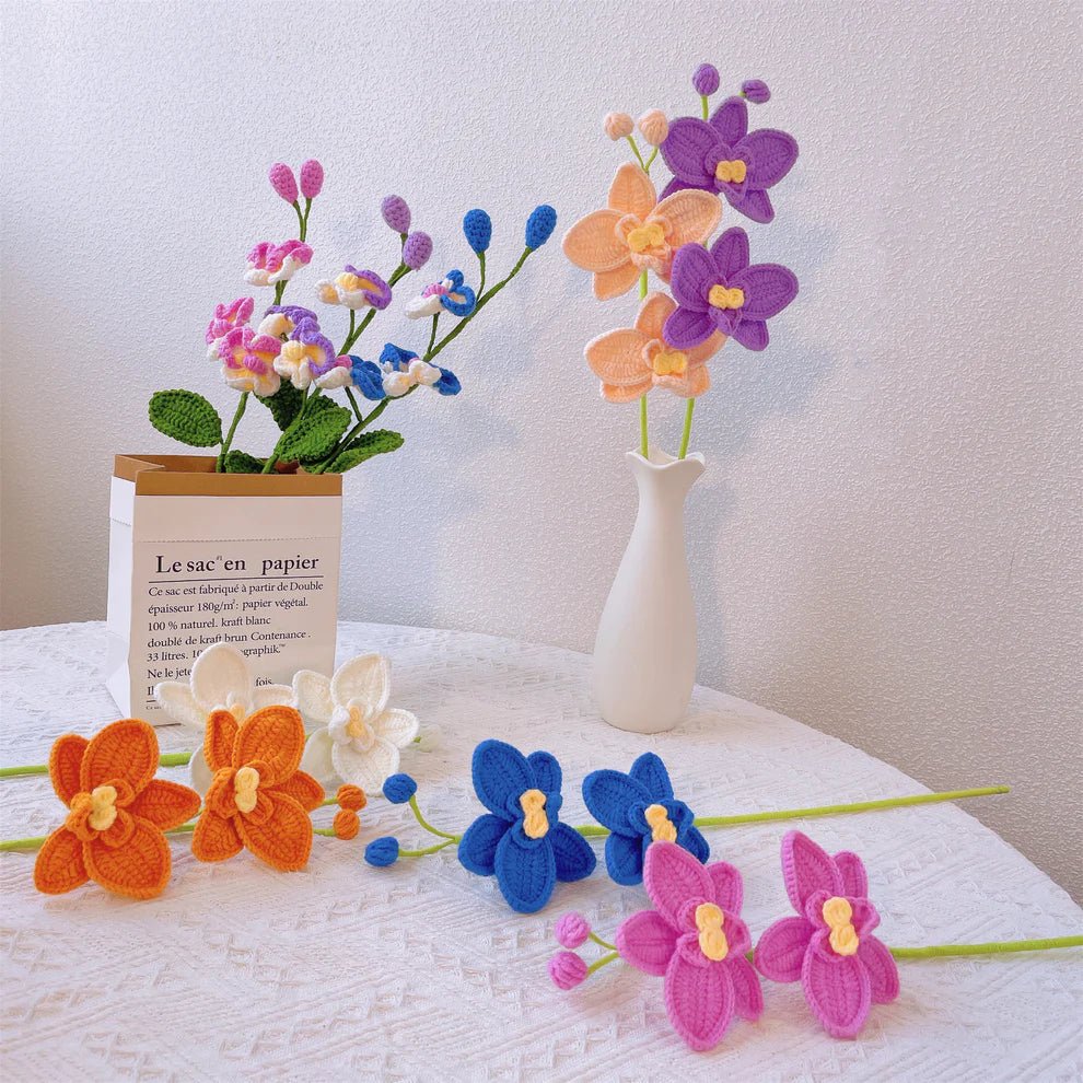 Crocheted orchids in vibrant colors arranged in paper bag and white vase on lace tablecloth