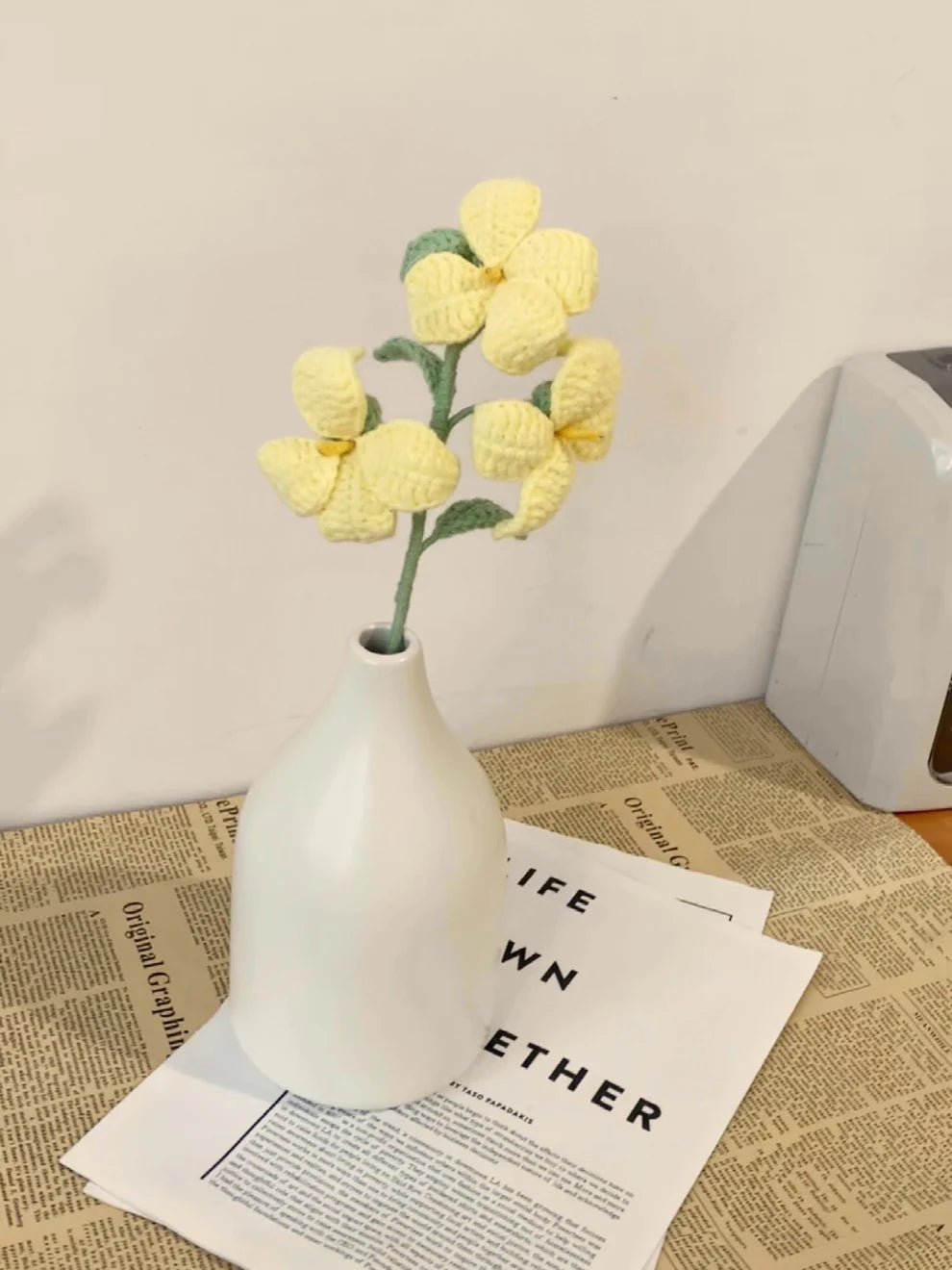 Crocheted yellow flowers in white vase on vintage newspaper with book page